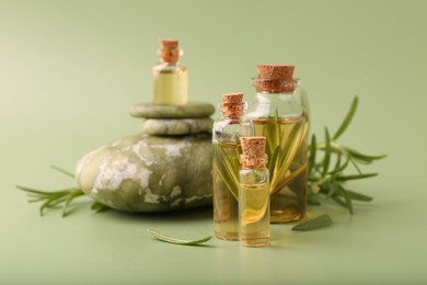 Aromatic essential oils in bottles, rosemary and pebble stones on green background