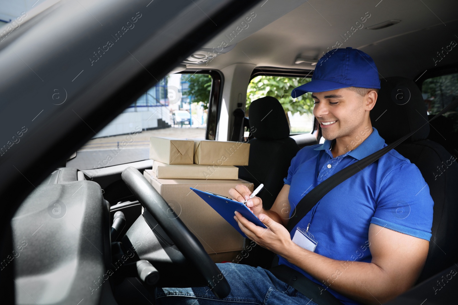 Photo of Young courier with parcels and clipboard in delivery car