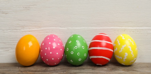 Photo of Decorated Easter eggs on table near wooden wall. Space for text