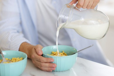 Making breakfast. Man pouring milk from jug into bowl with cornflakes at white marble table, closeup