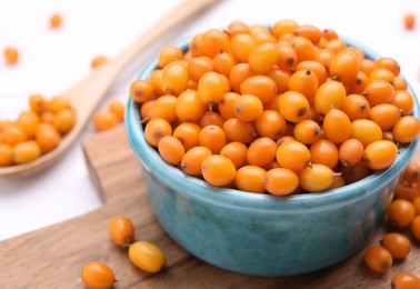 Photo of Bowl with fresh ripe sea buckthorn berries on wooden board, closeup