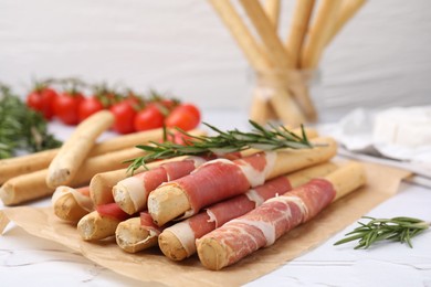 Delicious grissini sticks with prosciutto on white table, closeup