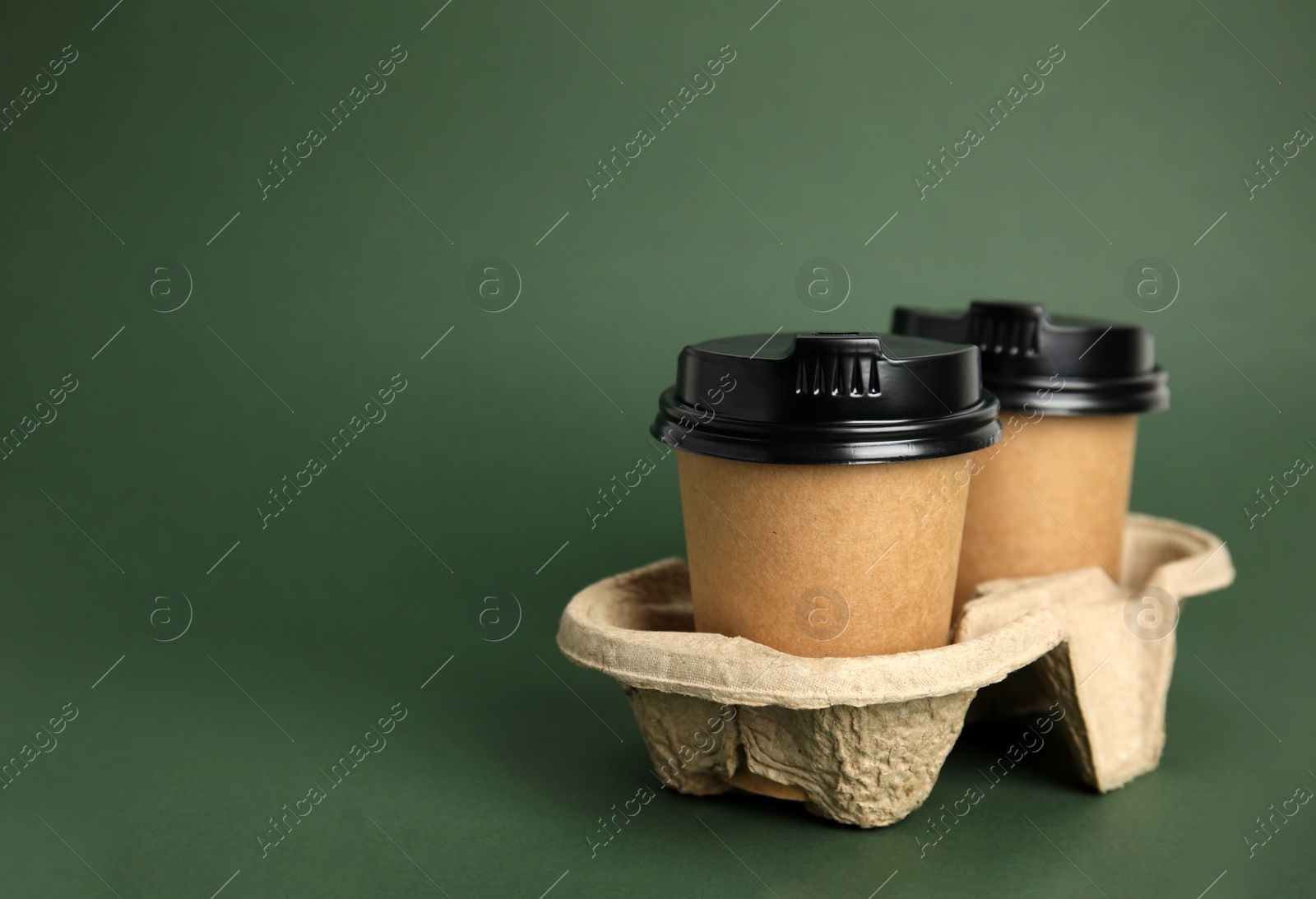 Photo of Takeaway paper coffee cups with plastic lids in cardboard holder on dark green background, space for text