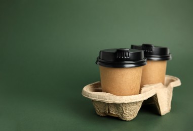 Takeaway paper coffee cups with plastic lids in cardboard holder on dark green background, space for text