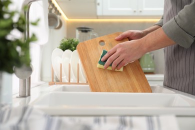 Photo of Man washing wooden cutting board at sink in kitchen, closeup