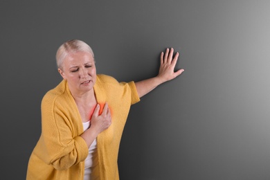 Mature woman having heart attack on color background