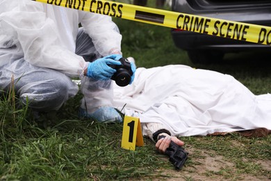 Photo of Criminologist taking photo of dead body at crime scene outdoors, closeup