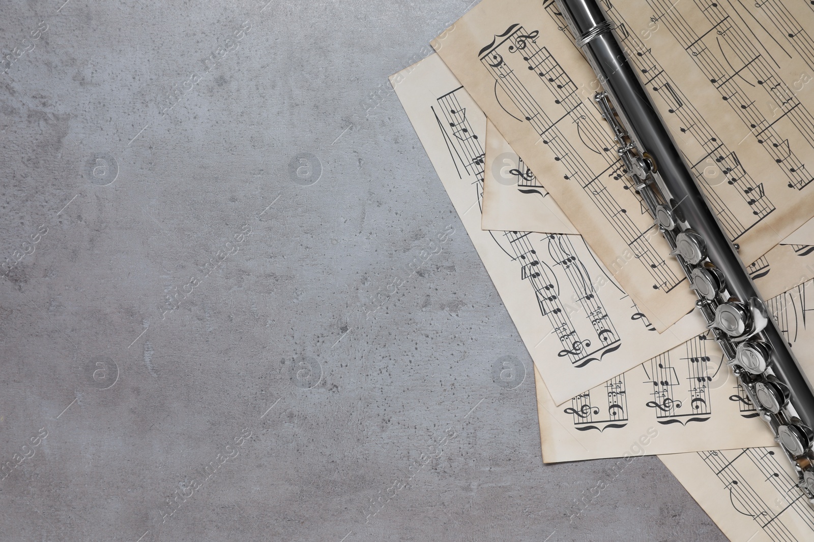 Photo of Sheets with musical notes and flute on grey table, flat lay. Space for text