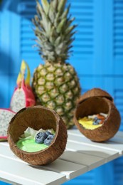 Photo of Tasty smoothie bowl served in coconut shells on white wooden table