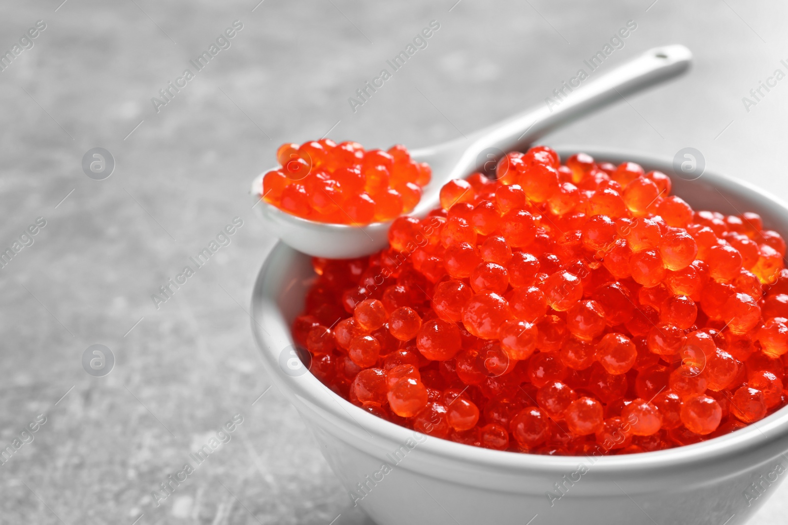 Photo of Ceramic bowl and spoon with delicious red caviar on table, closeup