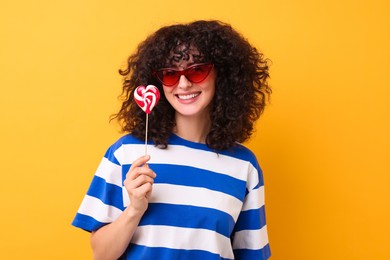 Beautiful woman in sunglasses with lollipop on yellow background