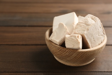 Photo of Bowl with pieces of compressed yeast on wooden table. Space for text