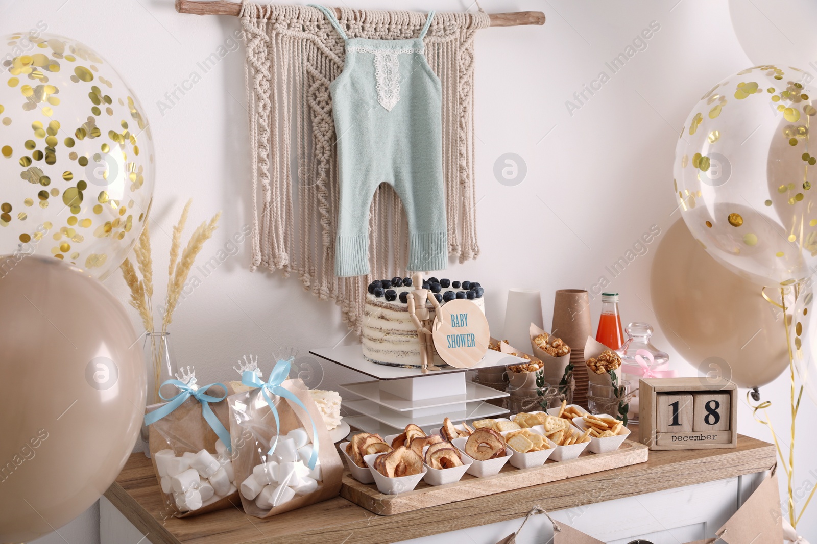 Photo of Baby shower party. Different delicious treats on wooden table and decor near light wall