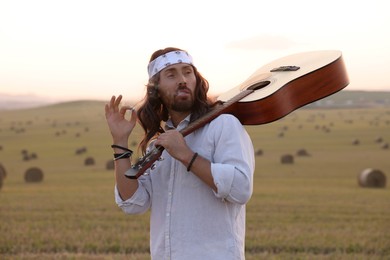 Photo of Stylish hippie man with guitar smoking joint in field