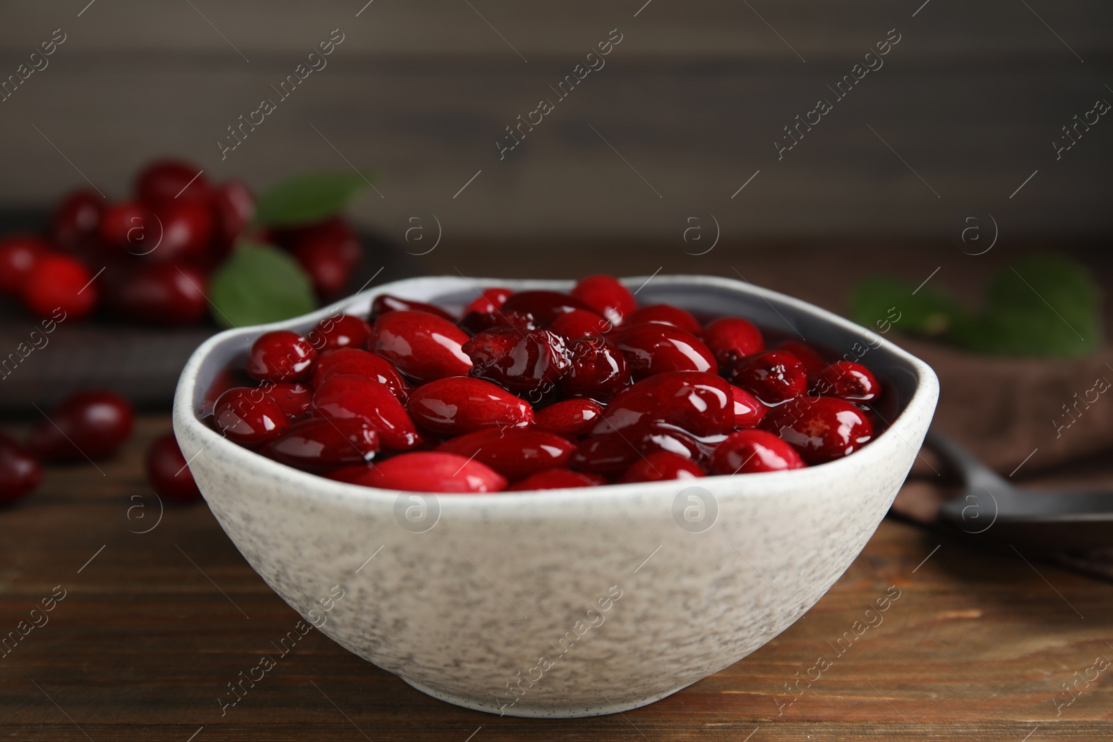 Photo of Delicious dogwood jam with berries in bowl on wooden table, closeup