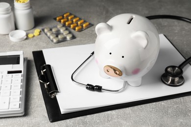 Photo of Piggy bank, stethoscope, calculator, clipboard and pills on light grey table. Medical insurance