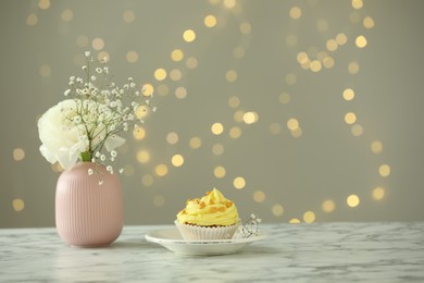 Delicious cupcake with yellow cream and flowers on white marble table against blurred lights