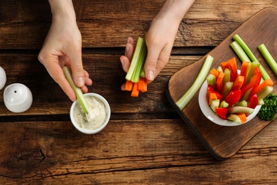 Woman dipping celery stick in sauce at wooden table, top view