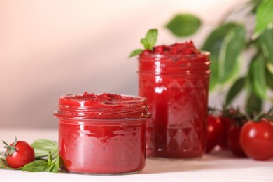Photo of Jars of tasty tomato paste and ingredients on white table, closeup. Space for text