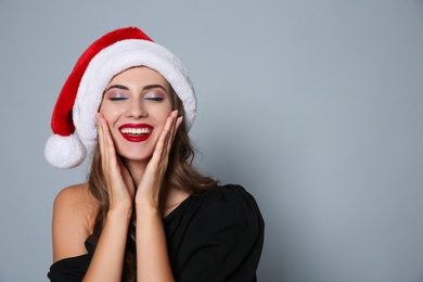 Photo of Happy woman in Santa hat on grey background, space for text. Christmas party