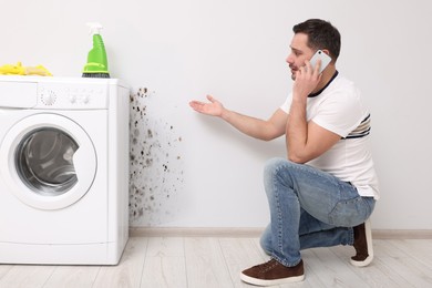 Mold removal service. Man talking on phone and looking at affected wall in bathroom