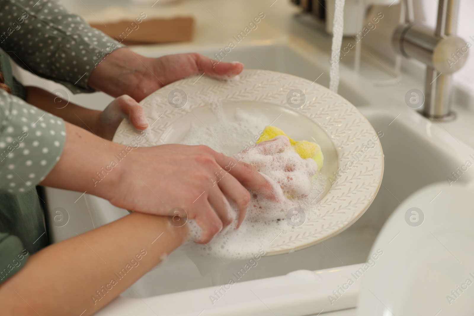 Photo of Mother and daughter washing plate above sink, closeup