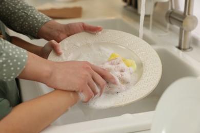 Photo of Mother and daughter washing plate above sink, closeup