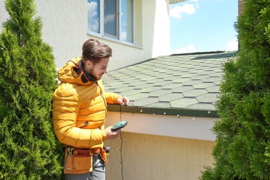 Young man decorating roof with Christmas lights