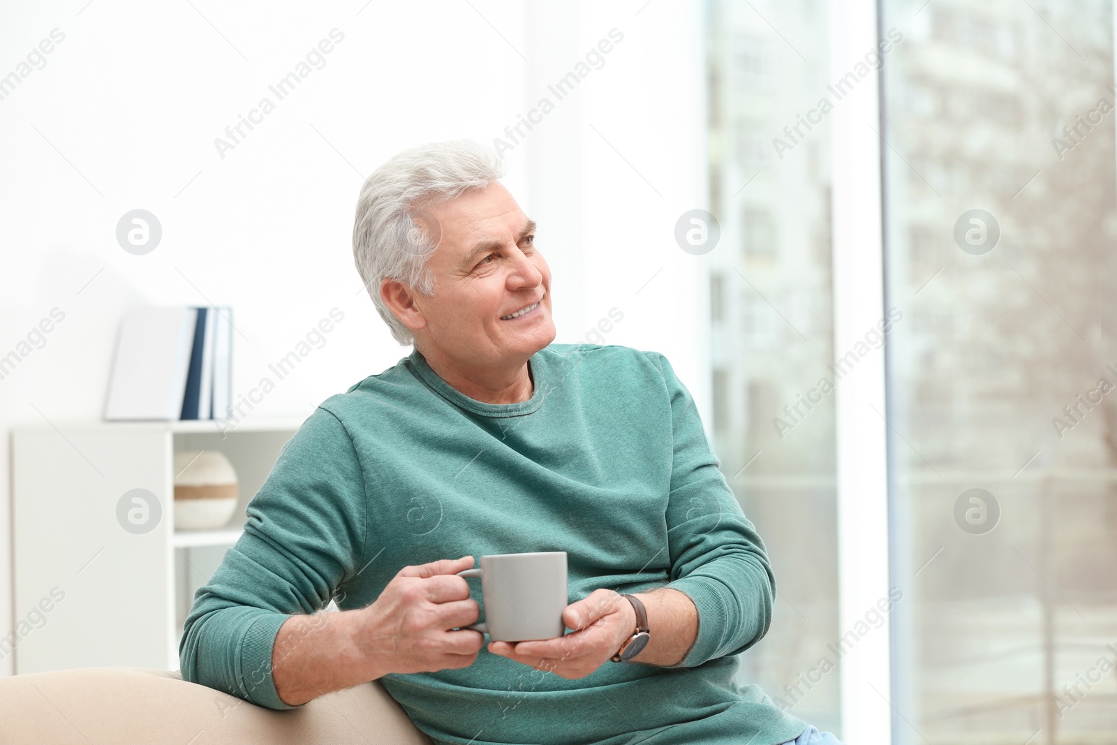 Photo of Portrait of mature man with cup of drink on sofa indoors