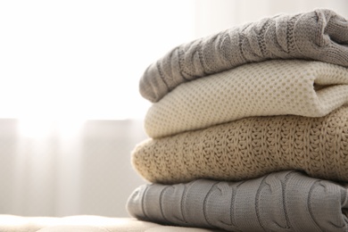 Photo of Stack of folded warm sweaters on couch indoors, closeup. Space for text