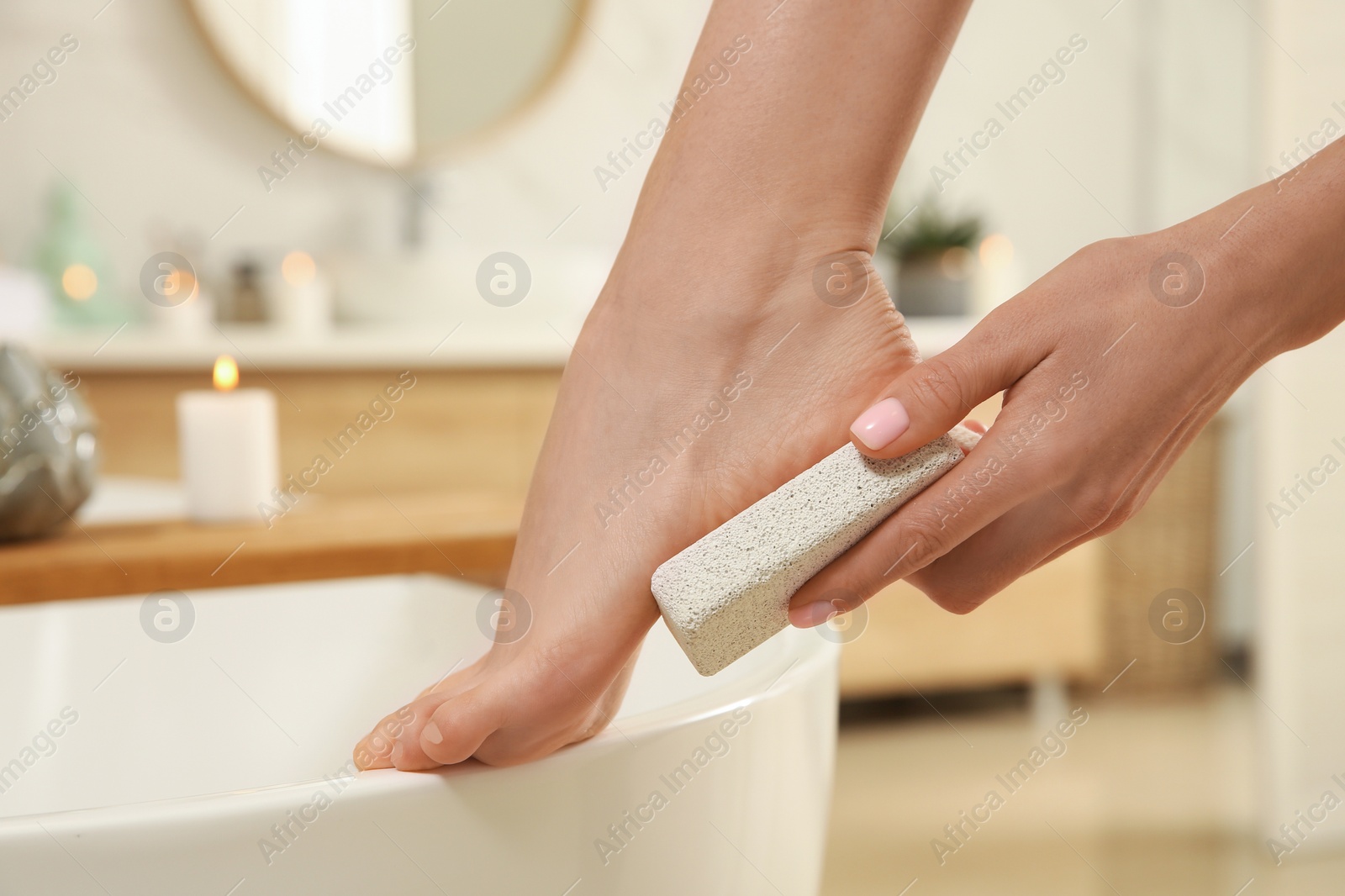 Photo of Woman using pumice stone for removing dead skin from feet in bathroom, closeup