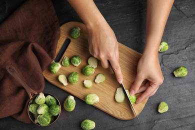 Woman cutting Brussels sprout at black slate table, top view