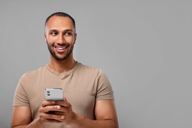 Photo of Happy man sending message via smartphone on grey background, space for text