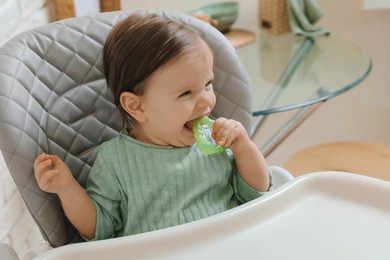 Photo of Cute little baby nibbling teether in high chair indoors