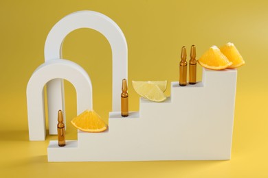 Photo of Stylish presentation of skincare ampoules with vitamin C and citrus slices on yellow background