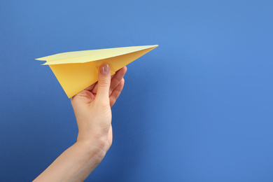 Photo of Woman holding paper plane on blue background, closeup. Space for text