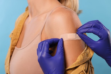 Photo of Nurse sticking adhesive bandage on woman's arm after vaccination on light blue background, closeup