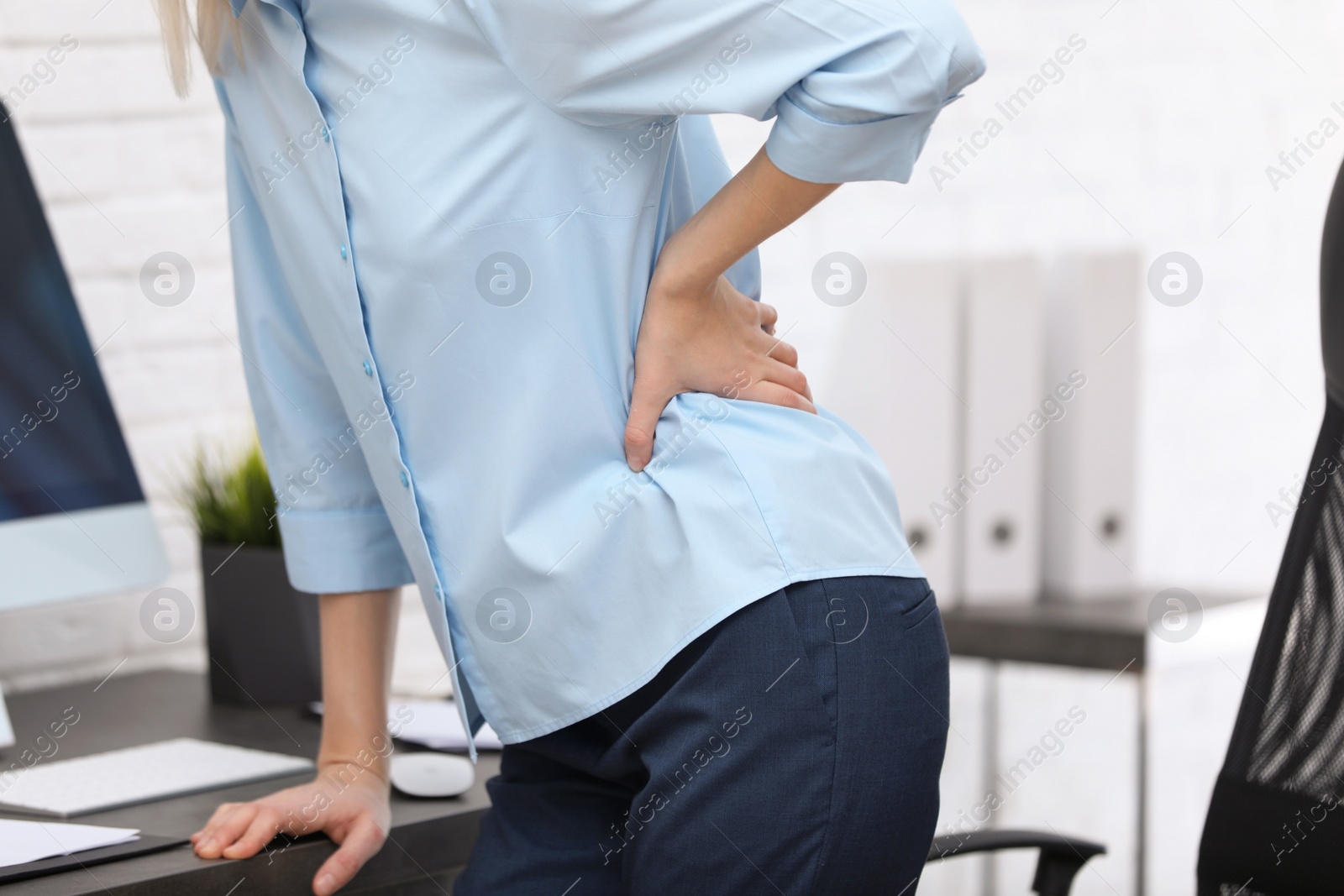 Photo of Young woman suffering from back pain in office, closeup