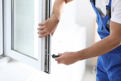 Construction worker repairing plastic window with screwdriver indoors, closeup