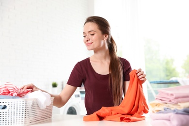 Photo of Happy woman with clean laundry at table indoors