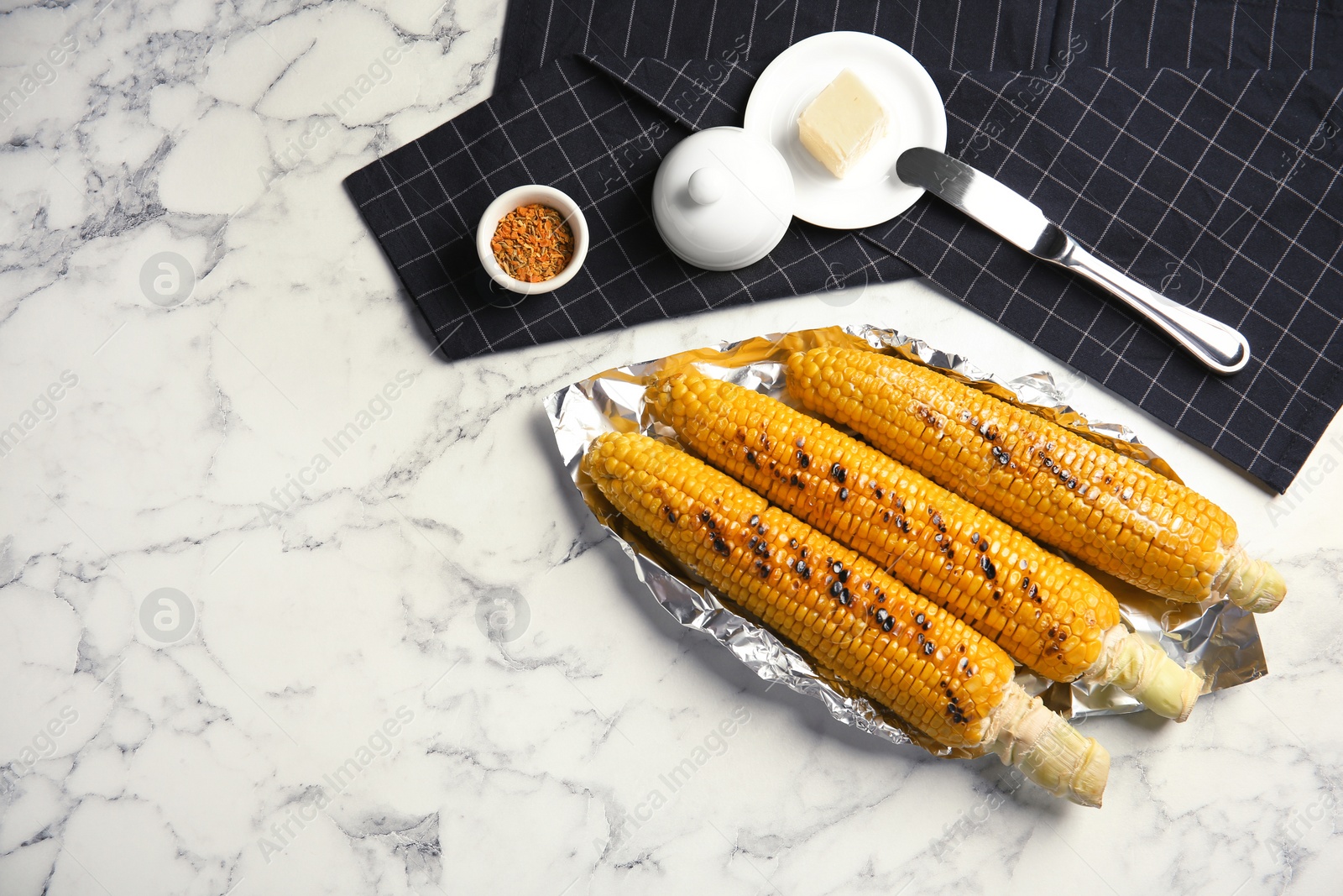 Photo of Fresh grilled tasty corn cobs served with butter on marble table, top view. Space for text