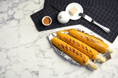 Fresh grilled tasty corn cobs served with butter on marble table, top view. Space for text