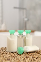 Photo of Mini bottles of cosmetic products on wicker mat against blurred background