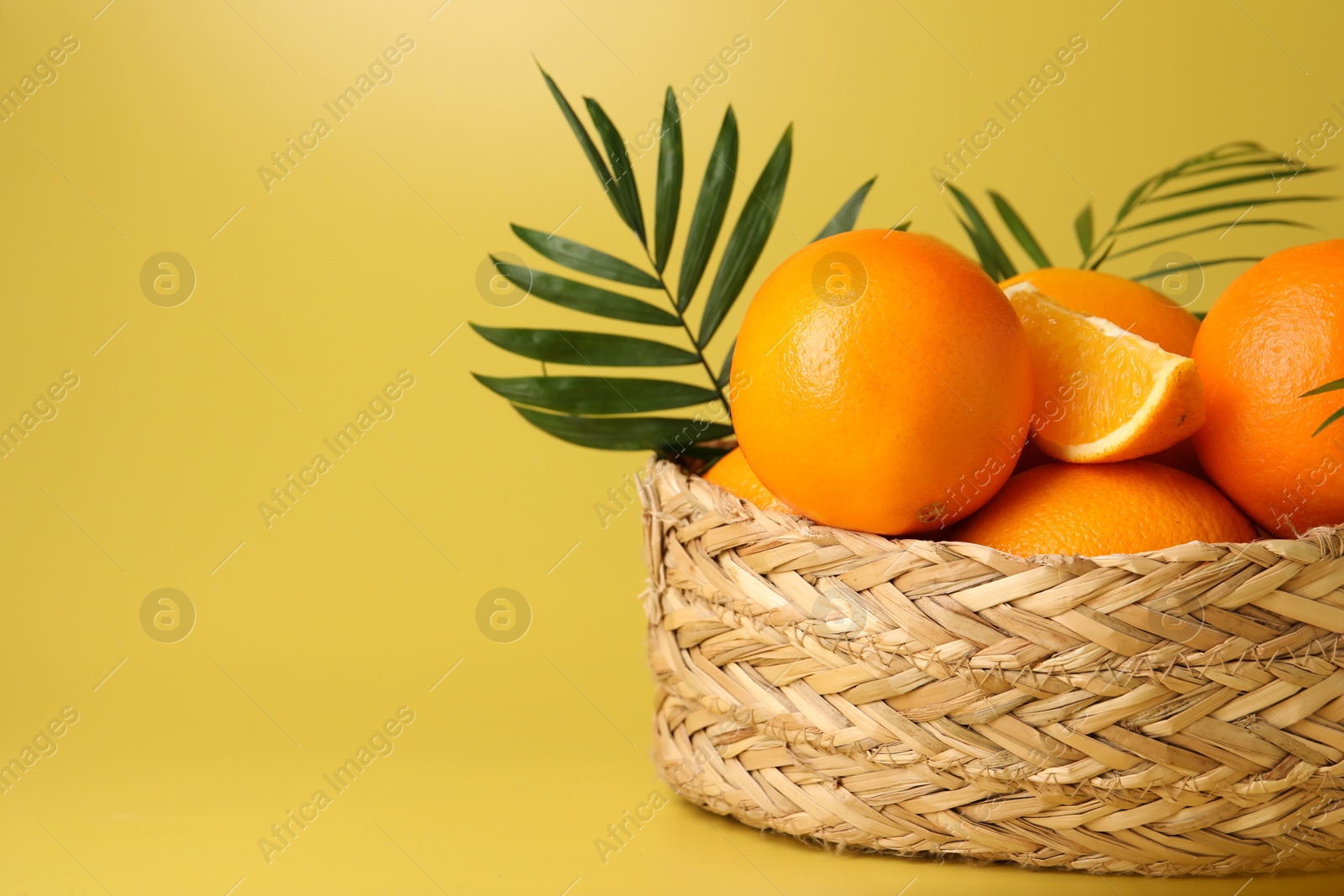 Photo of Fresh oranges in wicker basket on yellow background, closeup. Space for text