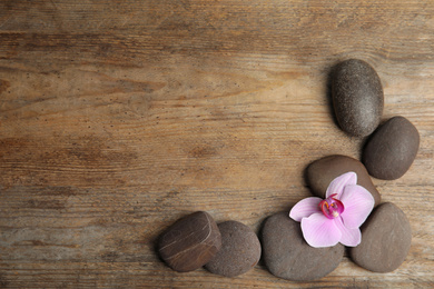 Stones with orchid flower and space for text on wooden background, flat lay. Zen lifestyle
