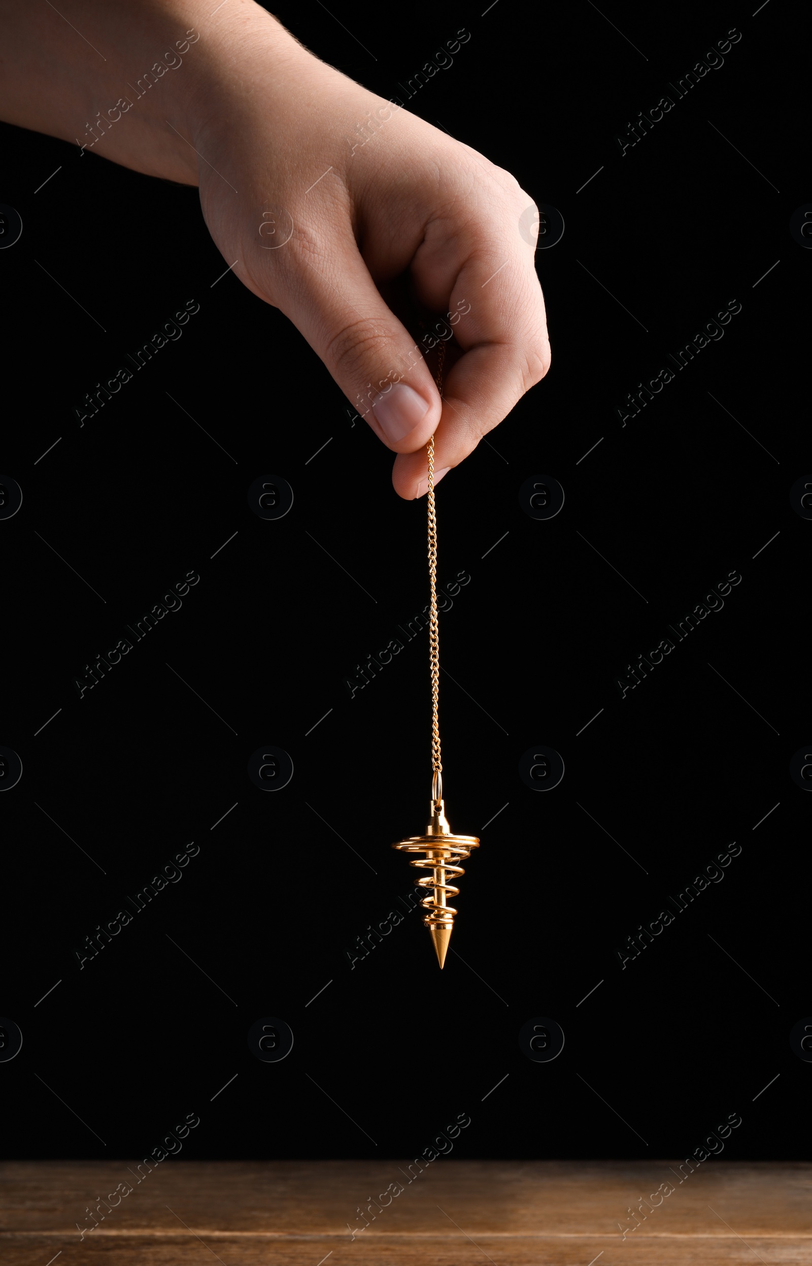 Photo of Psychotherapist with pendulum on black background, closeup. Hypnotherapy session