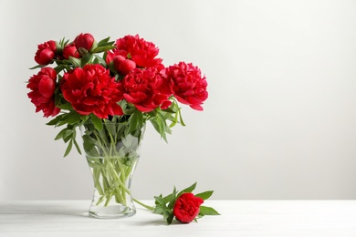 Vase with beautiful blooming peonies on table against light background