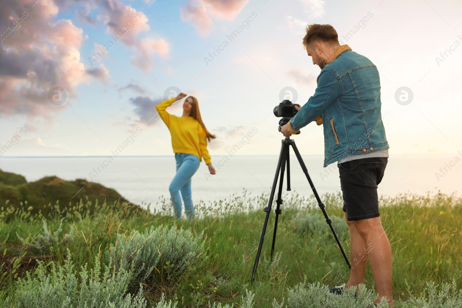 Photo of Male photographer taking picture of young woman with professional camera on green hill