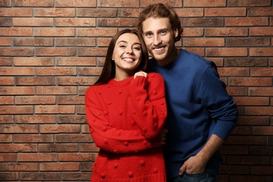 Photo of Young couple in warm sweaters near brick wall