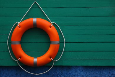 Photo of Orange lifebuoy hanging on green wooden board, space for text. Rescue equipment